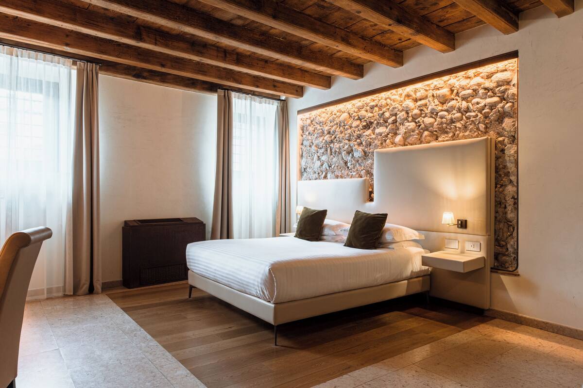 Une chambre moderne avec un grand lit, une table de chevet, une étagère intégrée au mur et un mur en pierre servant d’élément décoratif.