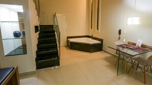 Une chambre d’hôtel moderne avec une table à manger en verre, un escalier noir, une baignoire et une cabine de douche en verre.