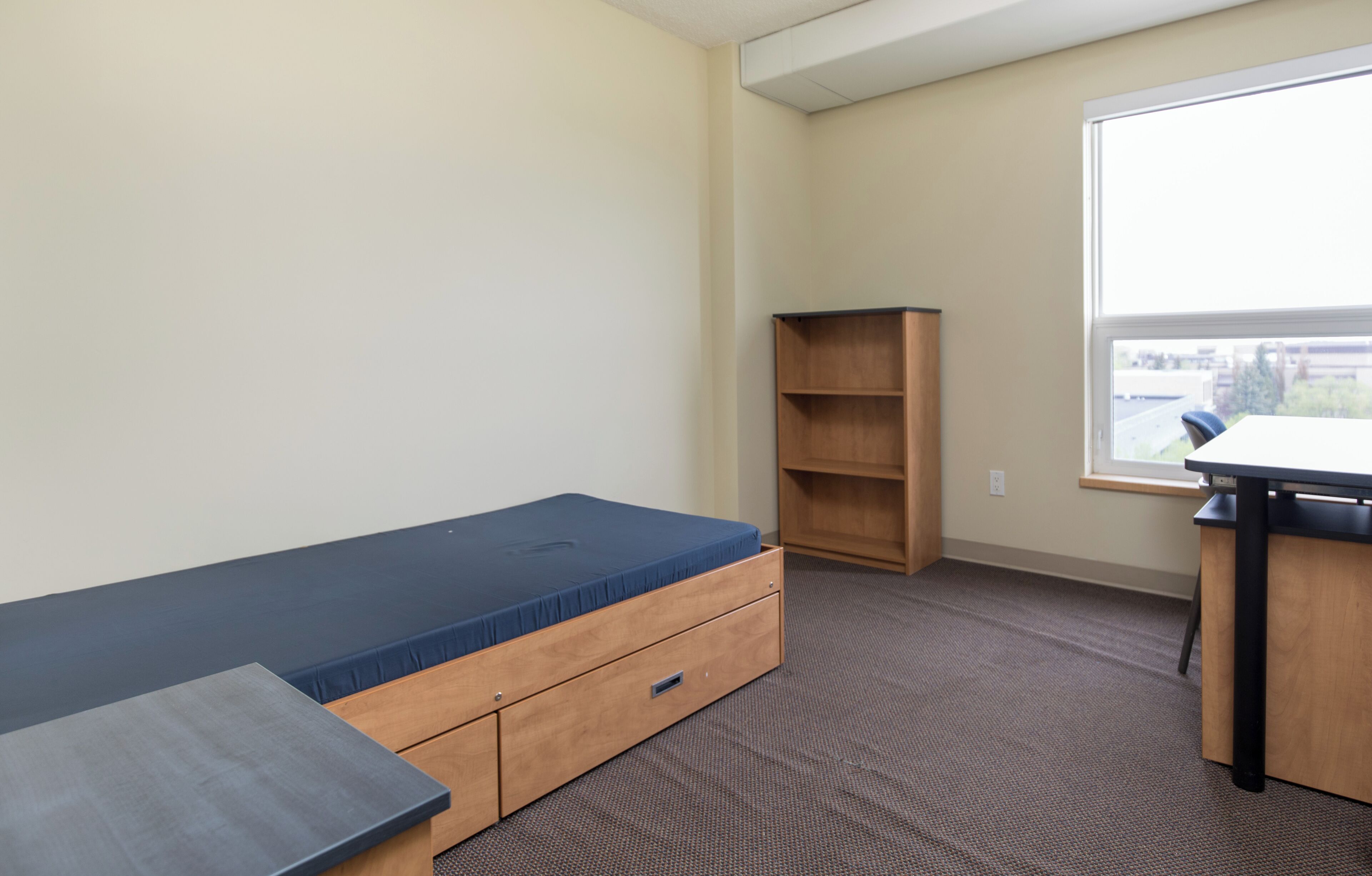 A room with a bed, a desk, a window, and a built-in shelf.