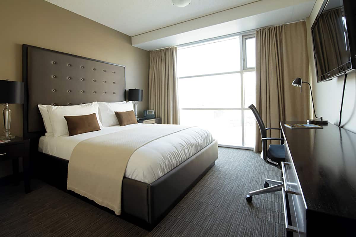 Une chambre d’hôtel avec un grand lit, un bureau, une chaise, une télévision et une fenêtre avec des rideaux.