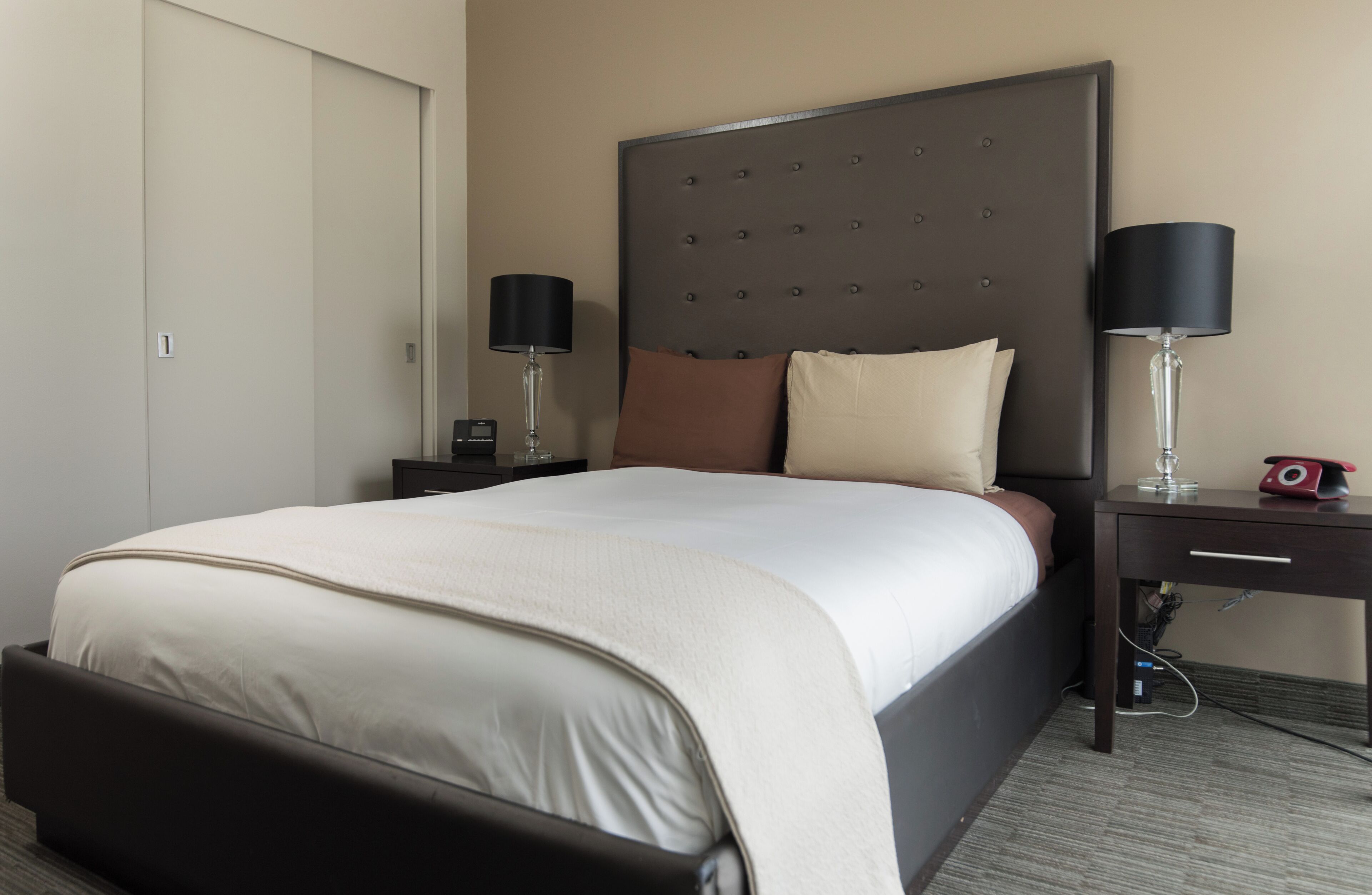 Una habitación de hotel con una cama grande, dos mesitas de noche, un florero y un teléfono rojo.