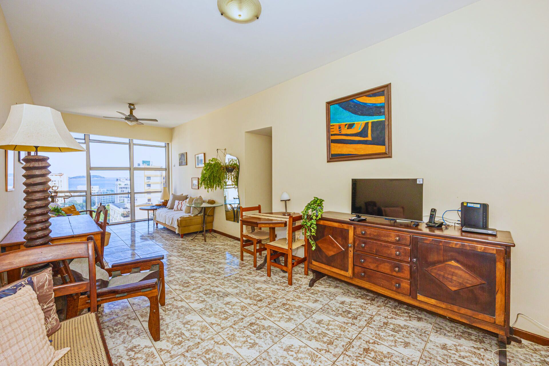 A spacious living room with a large window, a ceiling fan, a dining area, and a TV on a wooden cabinet.