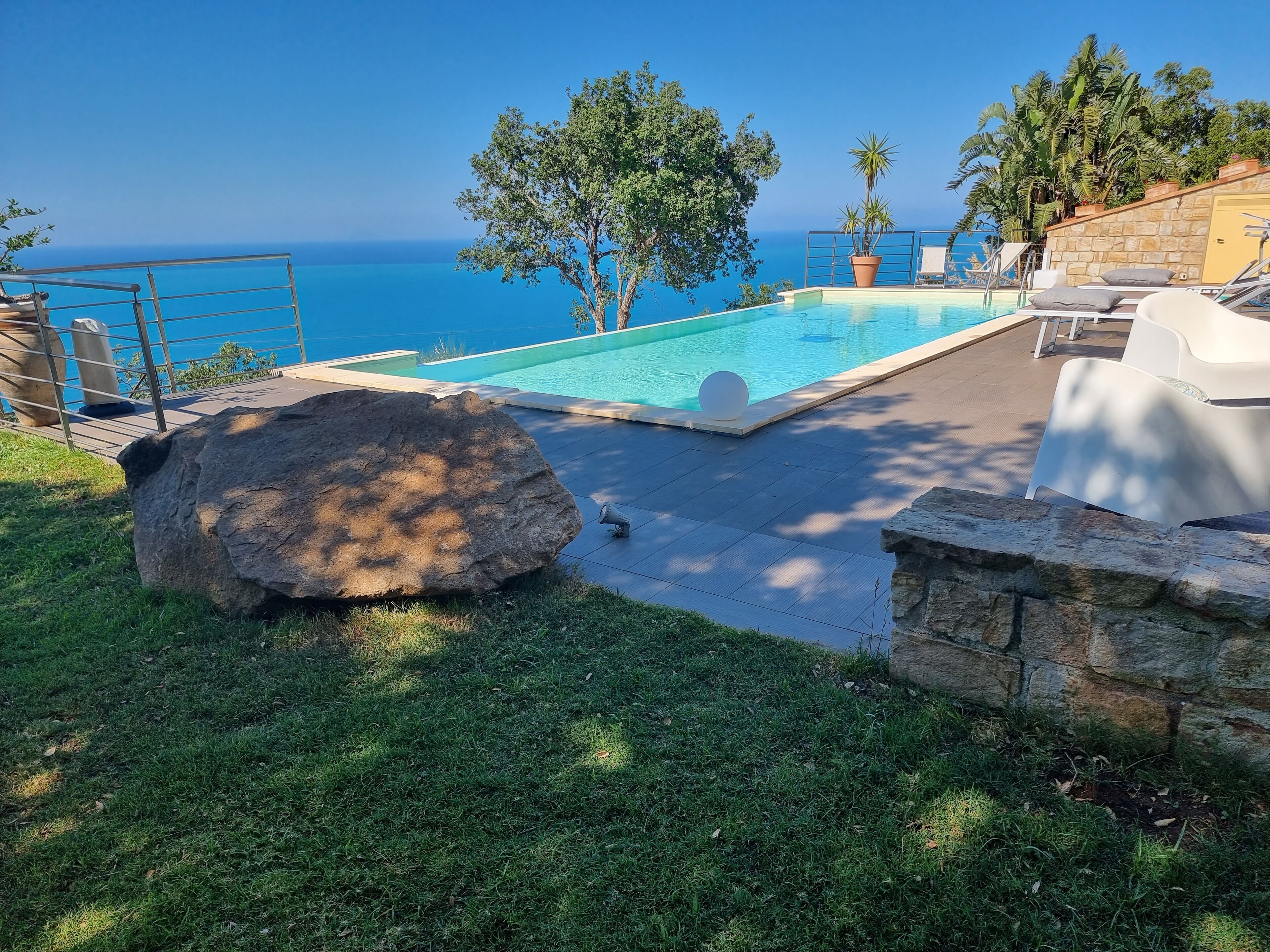 A swimming pool with a view of the ocean, surrounded by grass and rocks.