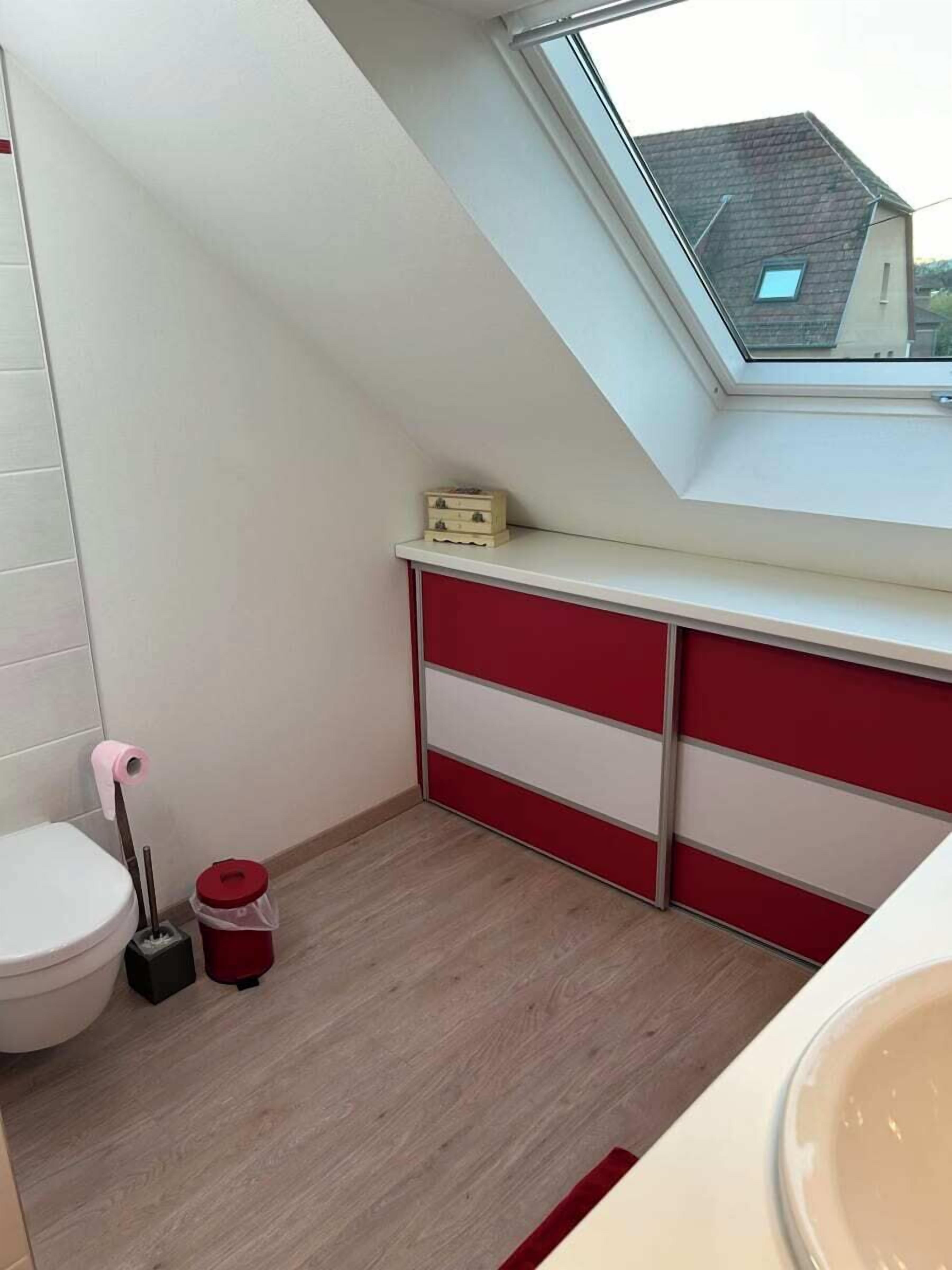 A small bathroom with a skylight, a toilet, a red and white cabinet, and a wooden floor.