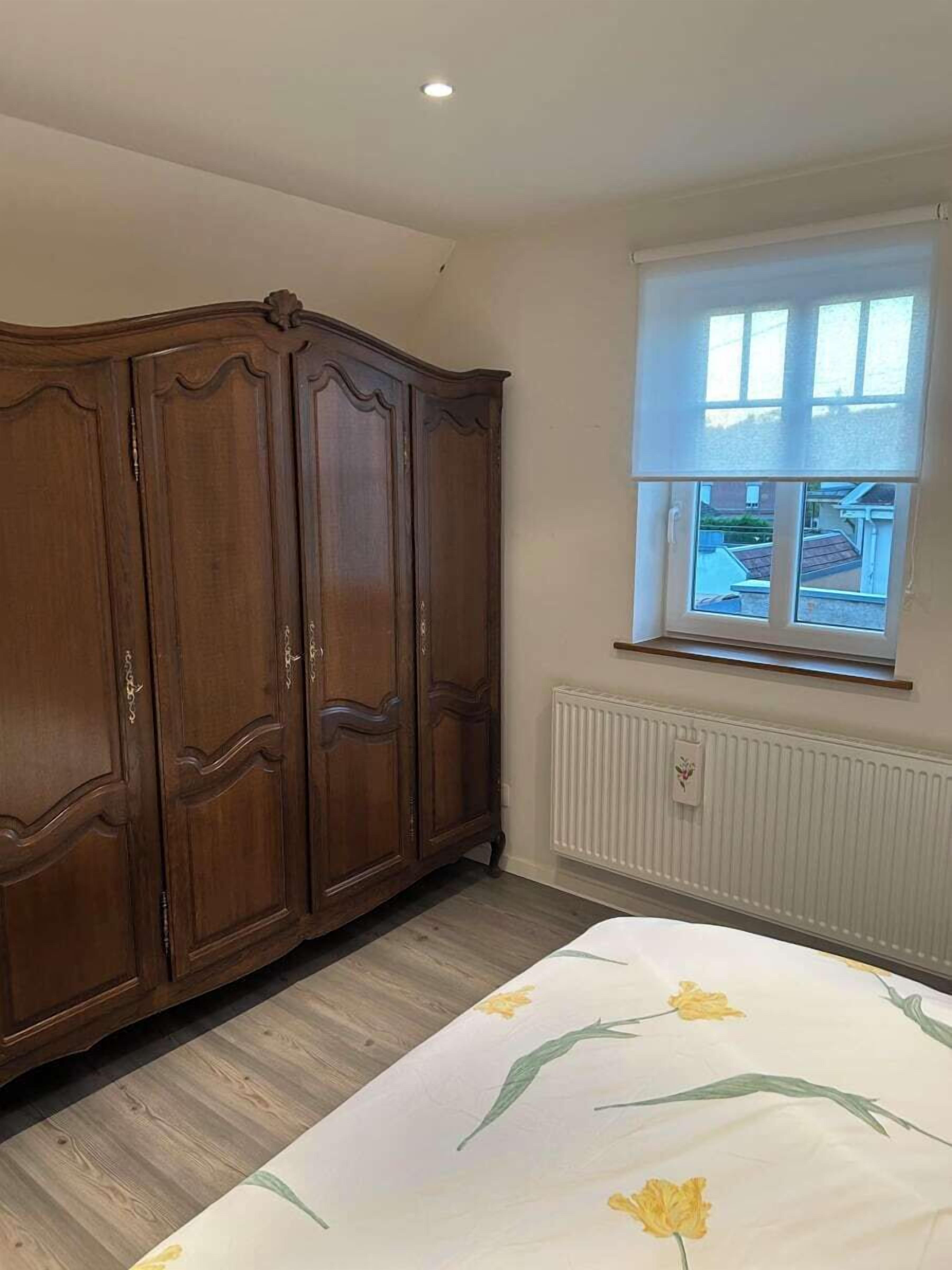 Ein Schlafzimmer mit großem Kleiderschrank, einem Fenster mit Jalousien und einer Heizung.