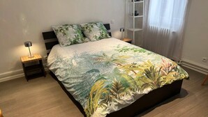 A bed with a floral bedspread, a bedside table with a lamp, and a nightstand. - Salutho (Selestat)