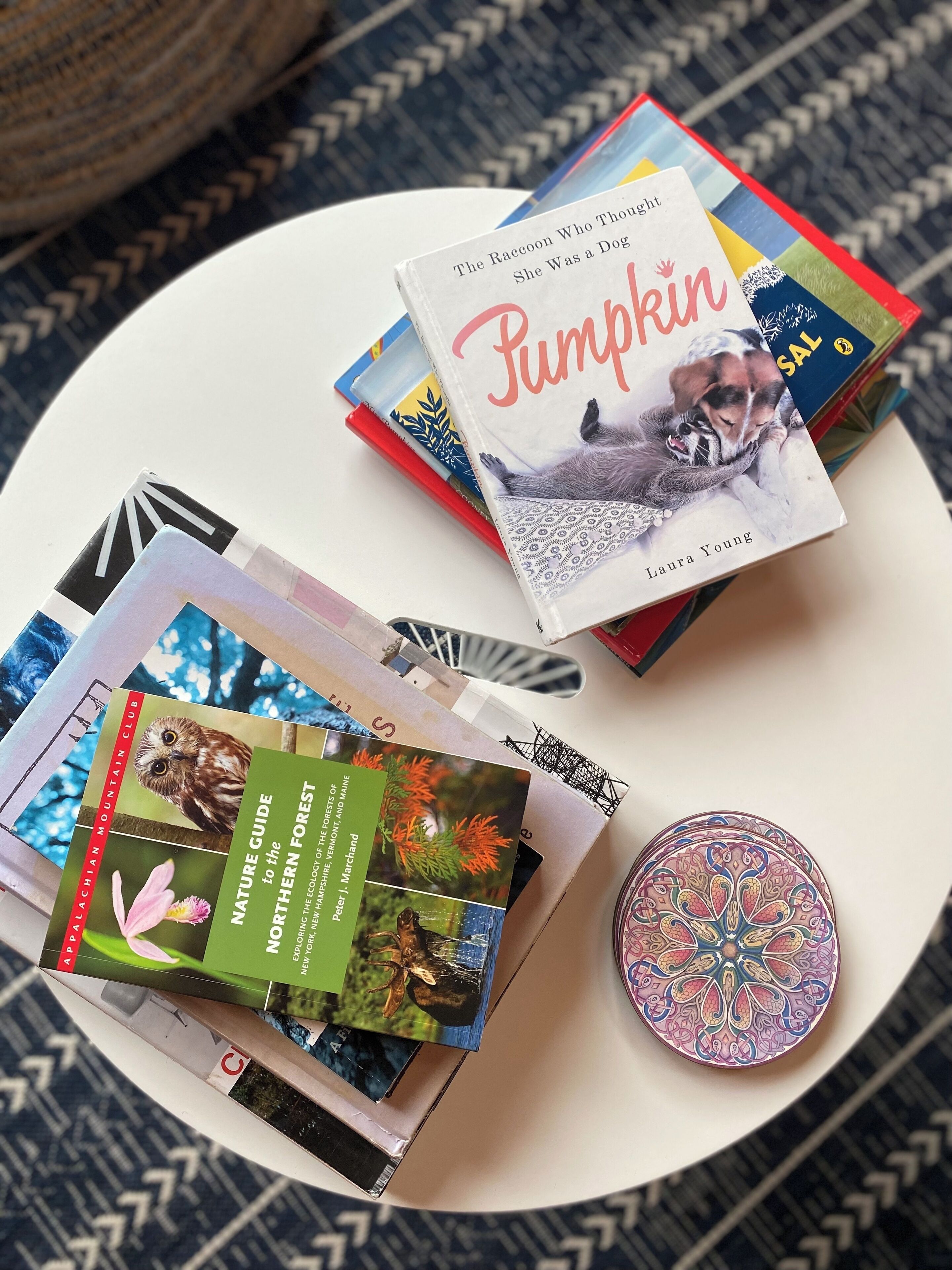 A stack of books on a white round table with a patterned tablecloth.