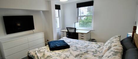 A bedroom with a bed, a desk, a chair, a television, and a window.