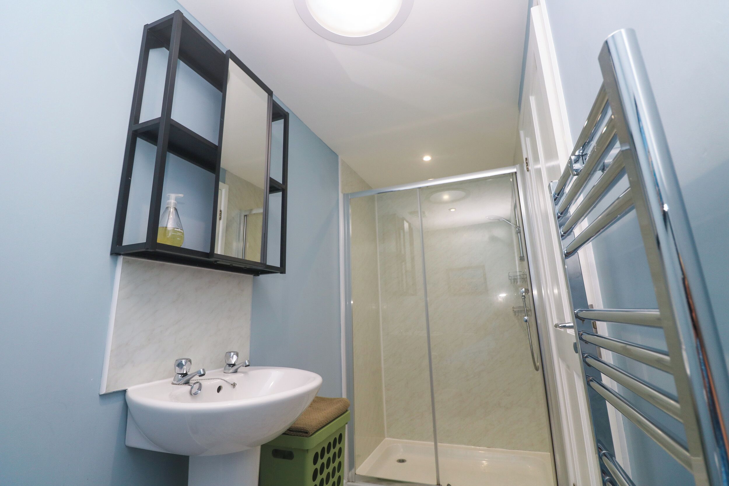Casa de banho com lavatório branco, espelho e cabine de duche em vidro.