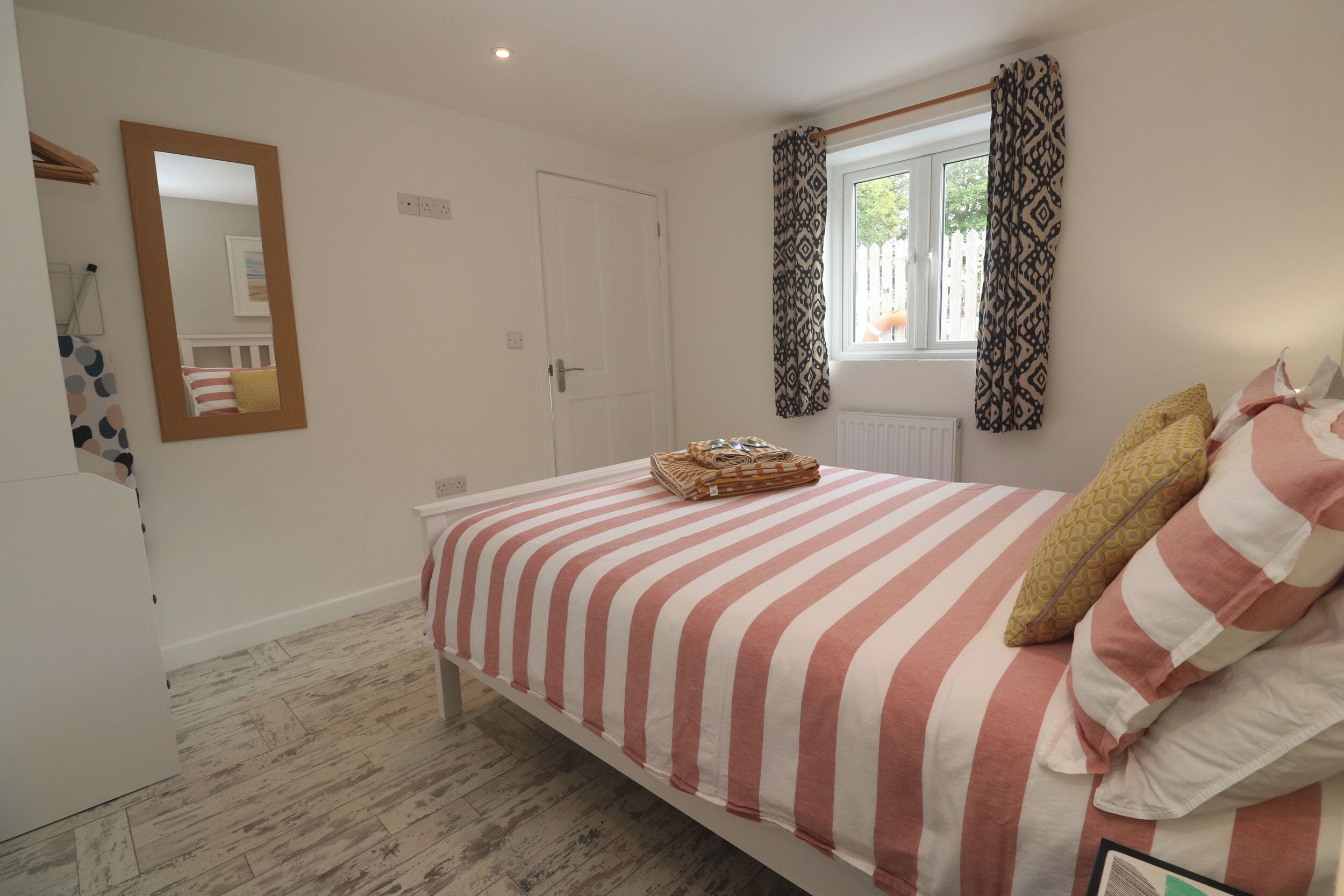 Un dormitorio con cama, ventana con cortinas estampadas, espejo y radiador.