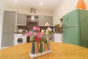 A kitchen with a wooden table, a green refrigerator, and a washing machine. - The Stable (Penzance)