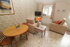 A cozy living room with a round wooden table, two sofas, a television, and a patterned wallpaper.