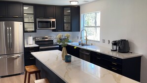 A modern kitchen with dark cabinets, stainless steel appliances, a marble island, and wooden stools. - Quiet 3BR NW Austin · Remote Work Ready · Pet Friendly (Austin)