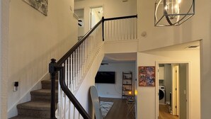 A multi-level home interior with a staircase, a chandelier, and a hallway leading to a laundry area. - Quiet 3BR NW Austin · Remote Work Ready · Pet Friendly (Austin)