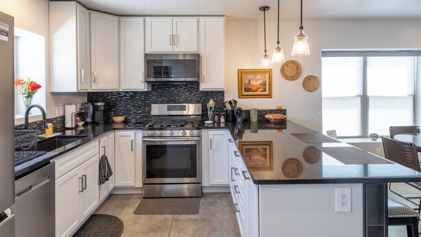 A modern kitchen with white cabinets, stainless steel appliances, a black countertop, and a large island.