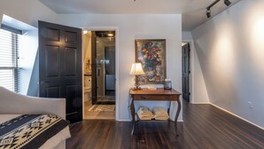 A modern living room with dark wood flooring, a black door, a glass shower, and a painting on the wall.