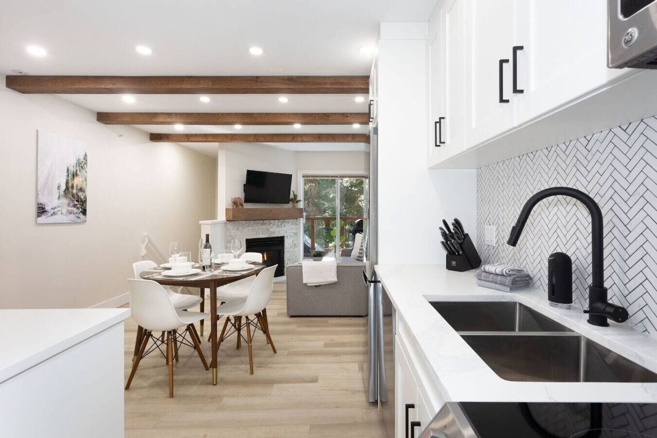 A modern kitchen with white cabinets, a black faucet, and a herringbone tile backsplash.