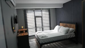 A modern bedroom with a bed, bedside table, lamp, and a large window with blinds. - Amed Sur Hotel (Diyarbakir)