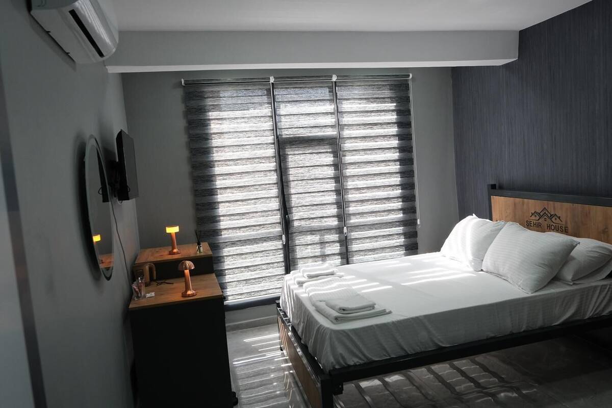 A modern bedroom with a bed, bedside table, lamp, and a large window with blinds.