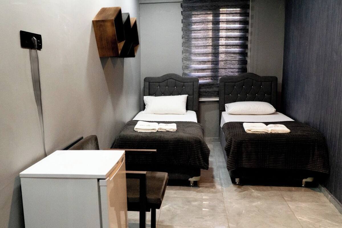 A small, compact room with two beds, a desk, and a chair.