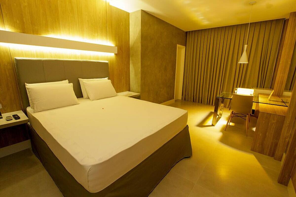 Una habitación de hotel con una cama grande, mesitas de noche, un escritorio con una silla y un espejo.