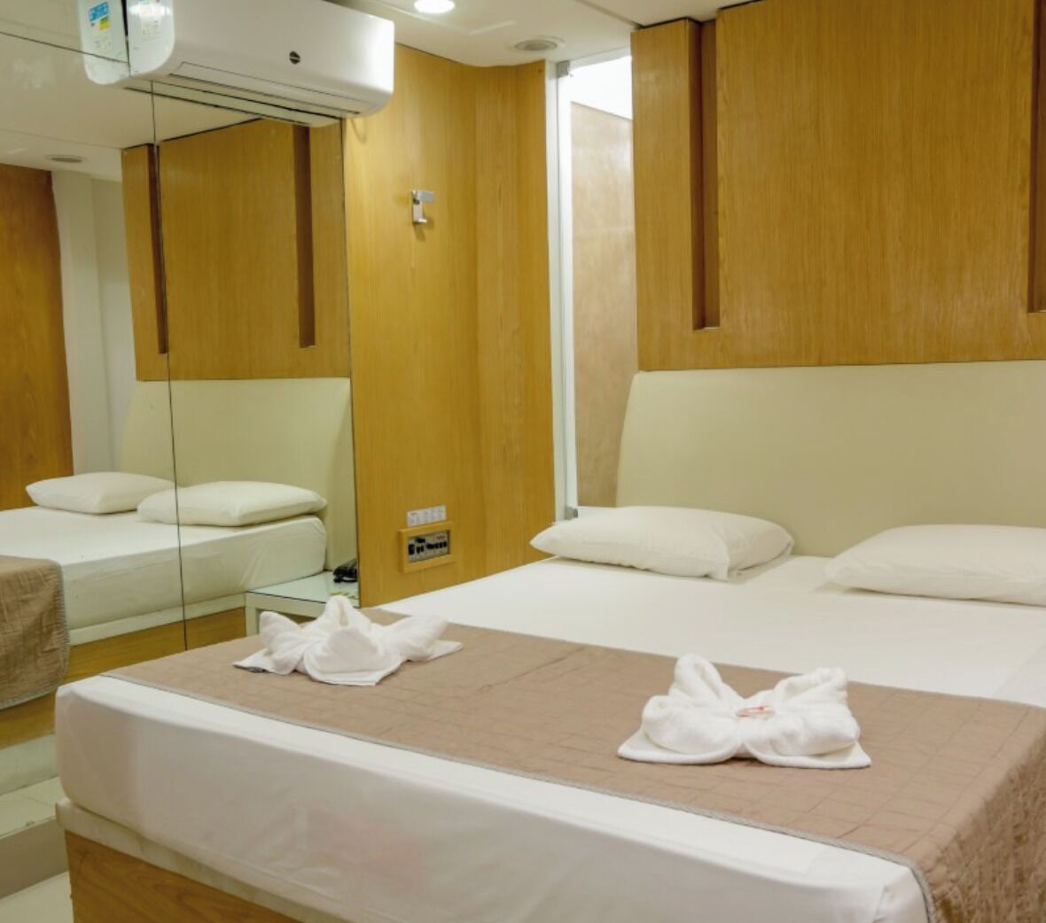 Habitación de hotel con una cama grande, una mesita de noche, un espejo y paneles de madera en las paredes.