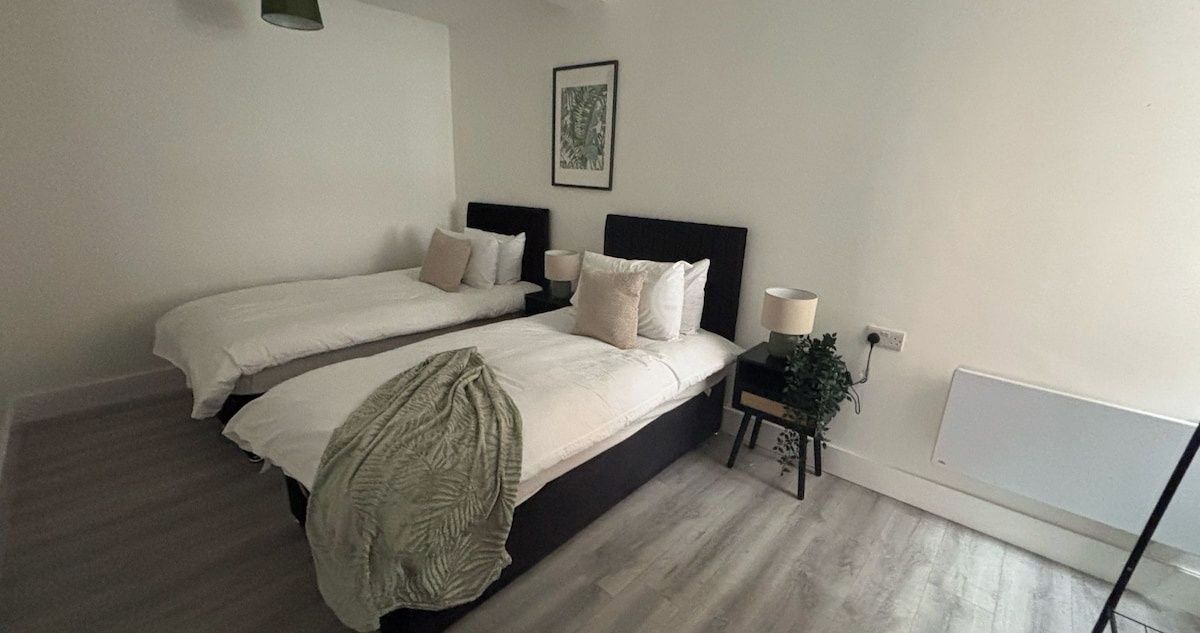 A bedroom with two beds, a nightstand with a lamp, and a wall-mounted picture.