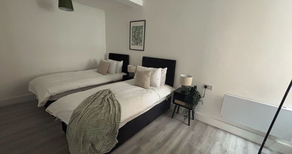 Une chambre avec deux lits, une table de chevet avec une lampe, un tableau accroché au mur et une fenêtre donnant sur un paysage.