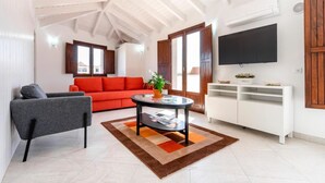 A living room with a high ceiling, a red sofa, a grey armchair, a round coffee table, and a white entertainment unit. - Loft located in the city center with a large terrace and good sun exposure (Tavira)