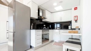 A modern kitchen with white cabinets, a stainless steel refrigerator, a built-in oven, and a small dining area with a bench. - Loft located in the city center with a large terrace and good sun exposure (Tavira)