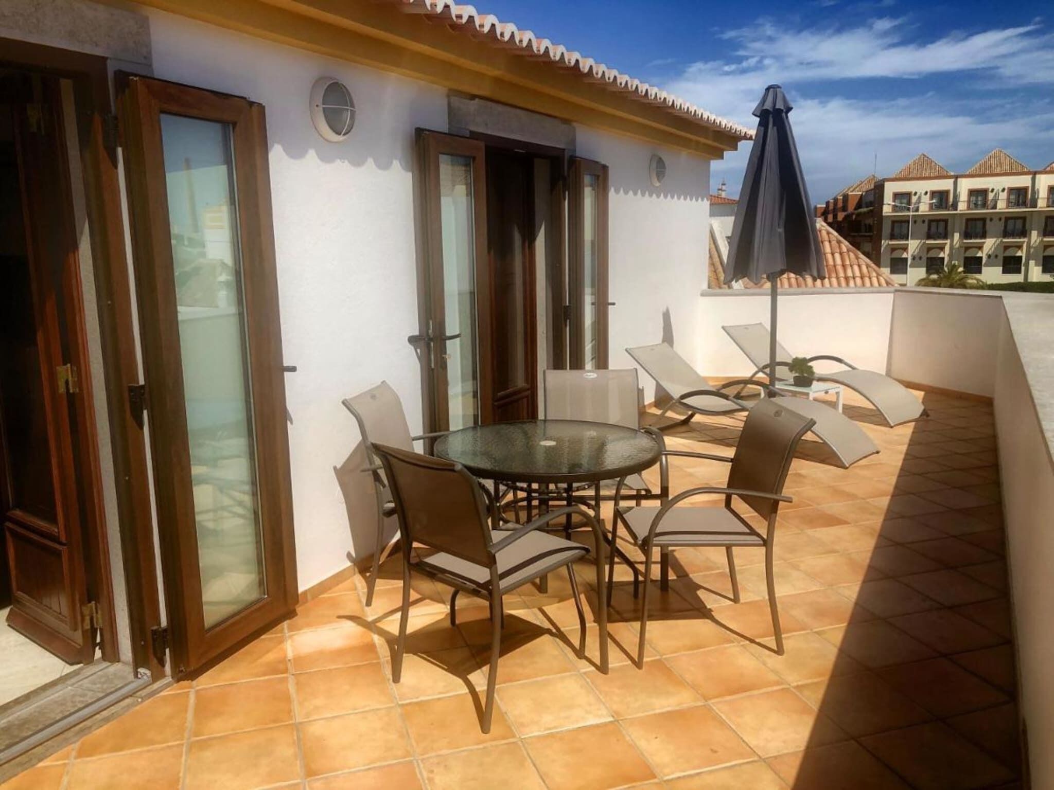 Un patio exterior con una mesa redonda y sillas, una puerta de cristal y un suelo de baldosas.