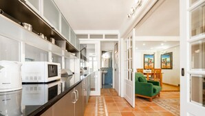 Une cuisine moderne dotée d’appareils électroménagers intégrés, un coin repas avec un canapé vert et un couloir menant à une salle de bain.