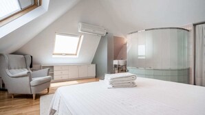Une chambre moderne avec un plafond en pente, un grand lit, une coiffeuse et une douche à parois courbes en verre.