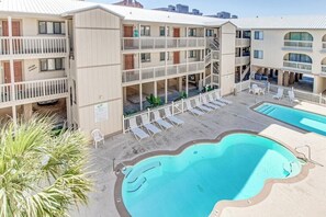 A multi-story hotel with balconies, a swimming pool, and lounge chairs.