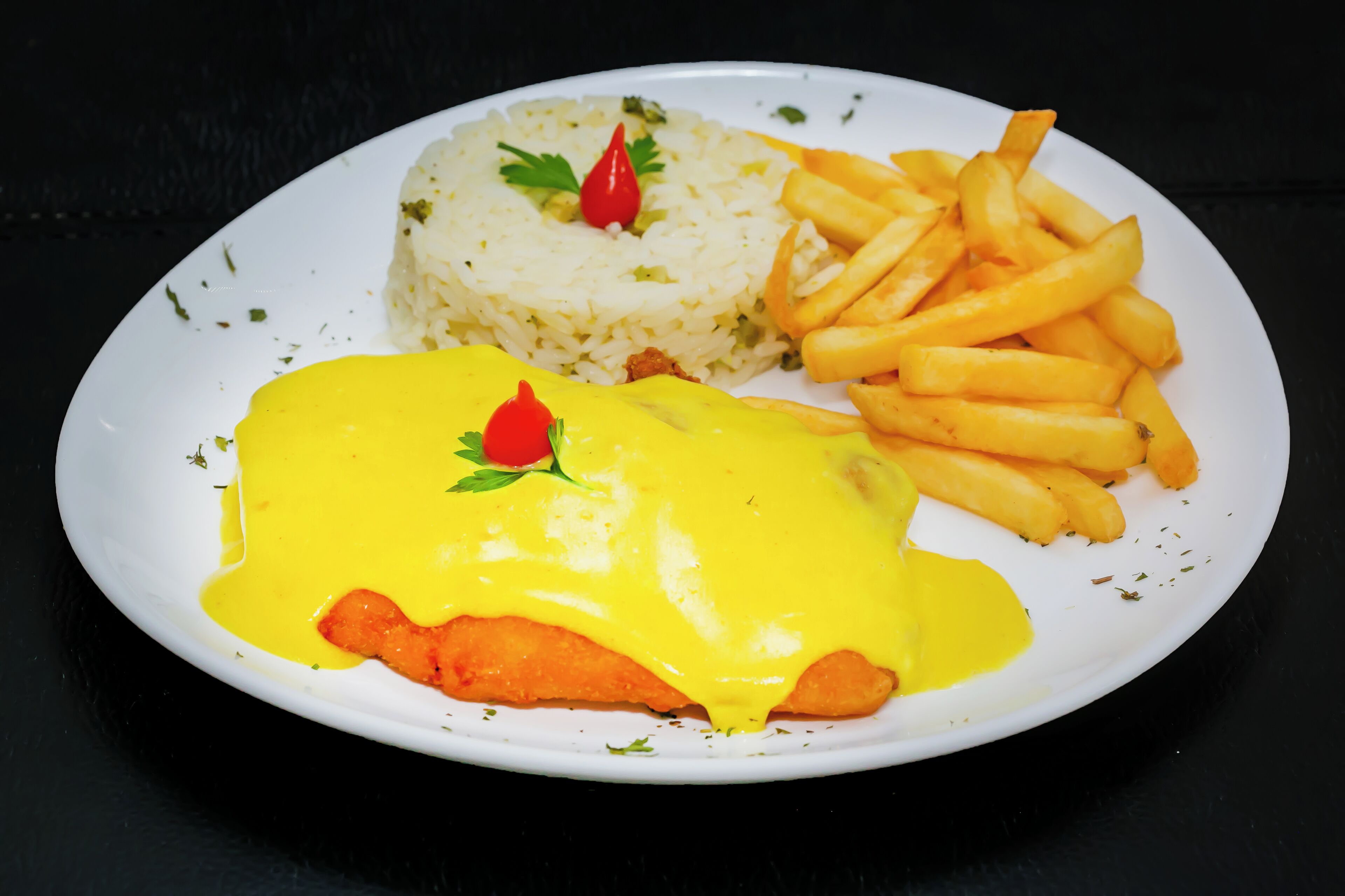 A plate with a fish fillet covered in yellow sauce, rice, and French fries.