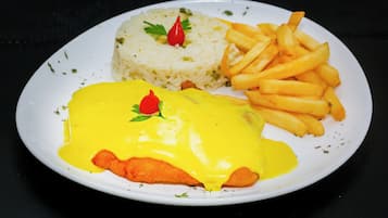 A plate with a fish fillet covered in yellow sauce, rice, and French fries.