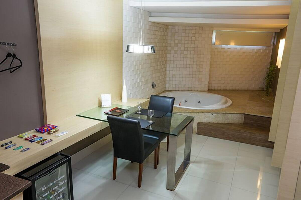 A modern bathroom with a glass shower enclosure, a bathtub, and a glass table with chairs.