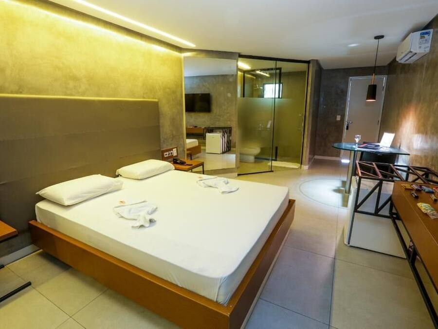 A modern hotel room with a large bed, a desk, and a glass-enclosed shower area.