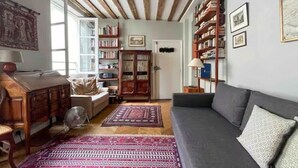 Una sala de estar acogedora con un sofá, una mesa de centro de madera, una estantería y una alfombra estampada.