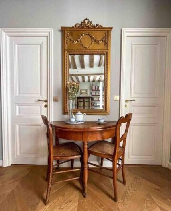 A dining room with a round wooden table, two chairs, a mirror with a decorative frame, and white double doors.
