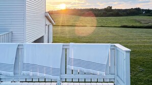 Un terrazzo con ringhiere bianche e vista su un prato e un tramonto.