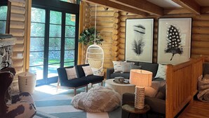 L'intérieur d'un chalet confortable, avec un plafond en bois, un canapé, un fauteuil, un luminaire suspendu et des œuvres d'art encadrées accrochées au mur.