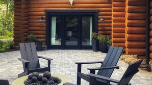 Une cabane en rondins avec une cheminée, deux fauteuils Adirondack et un espace patio.