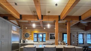 Une cuisine spacieuse avec des poutres en bois, un grand îlot central doté de tabourets et un réfrigérateur en acier inoxydable.