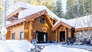 Une cabane en rondins avec des fondations en pierre, un revêtement extérieur en bois et un espace extérieur aménagé avec des sièges sous une véranda.