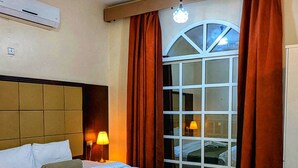 A hotel room with a bed, a ceiling fan, an air conditioner, a window with curtains, and a view of the outside. - Coral Bay Hotel Khorfakkan (Khor Fakkan)