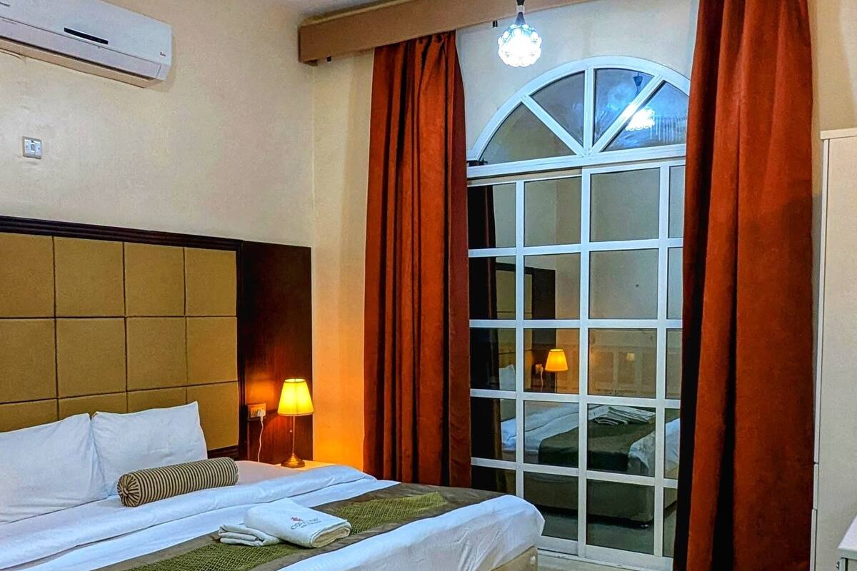 Une chambre d’hôtel équipée d’un lit, d’un ventilateur de plafond, d’un climatiseur, d’une fenêtre avec des rideaux et offrant une vue sur l’extérieur.