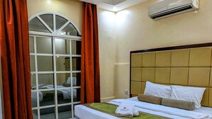 A hotel room with a large bed, a window with curtains, an air conditioning unit, and a tiled floor. - Coral Bay Hotel Khorfakkan (Khor Fakkan)