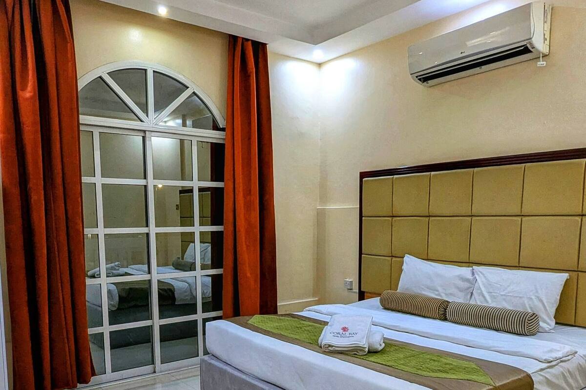 Une chambre d’hôtel avec un grand lit, une fenêtre avec des rideaux, un appareil de climatisation et un sol carrelé.