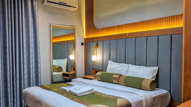 A modern hotel room with a large bed, a wooden headboard, a bedside table, a mirror, and a ceiling light. - Coral Bay Hotel Khorfakkan (Khor Fakkan)